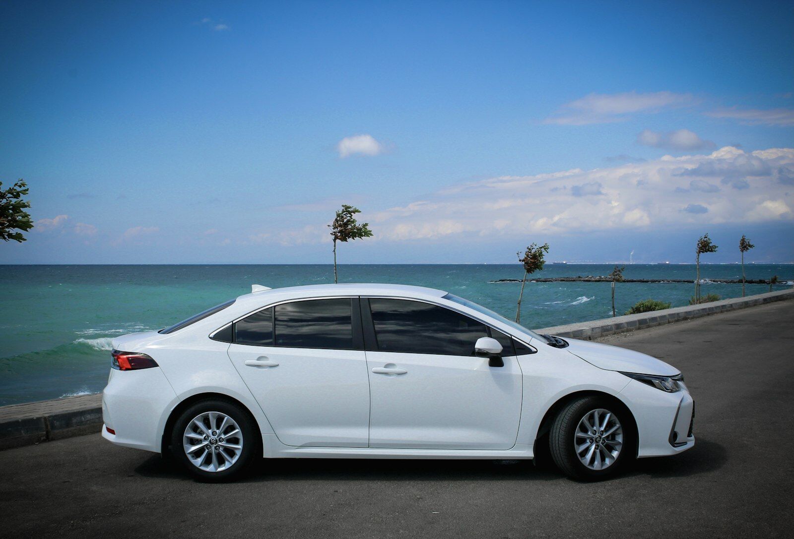 A white sedan parked on a coastal road beside a turquoise sea